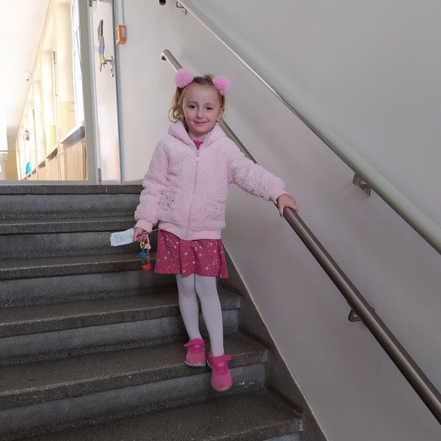 Na zdjęciu widać dziewczynkę, która stoi na schodach i trzyma się poręczy 